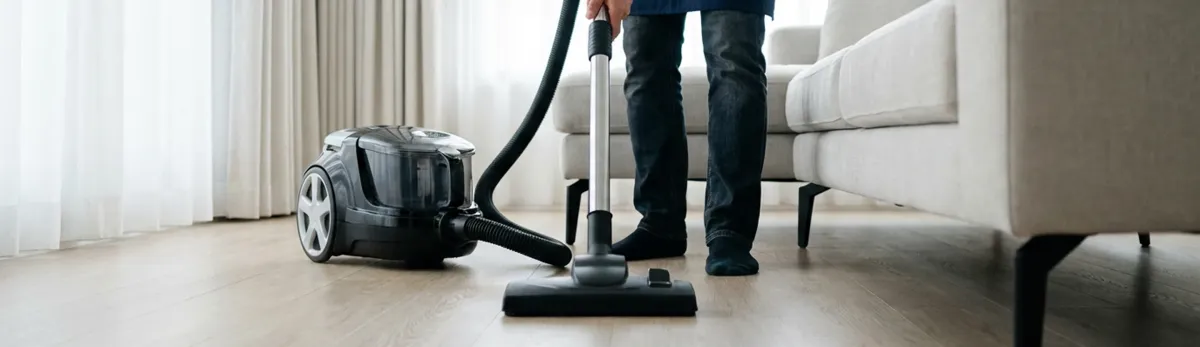 Professional house cleaner vacuuming a living room floor with a canister vacuum cleaner, Indianapolis, IN.