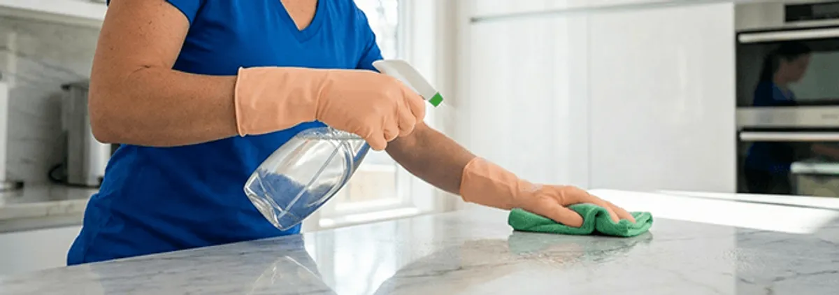 Maid service worker spraying and wiping a kitchen countertop with a microfiber cloth for sanitizing, Indianapolis, IN.