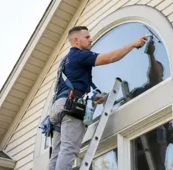 Professional window cleaner on a ladder using a squeegee to clean an exterior arched window, Indianapolis, IN.